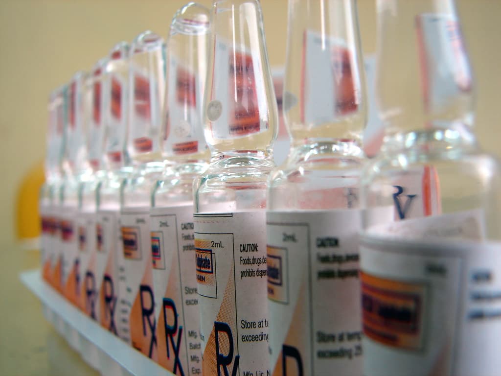 Fileira de frascos de medicamento com etiquetas, fotografados de perto.