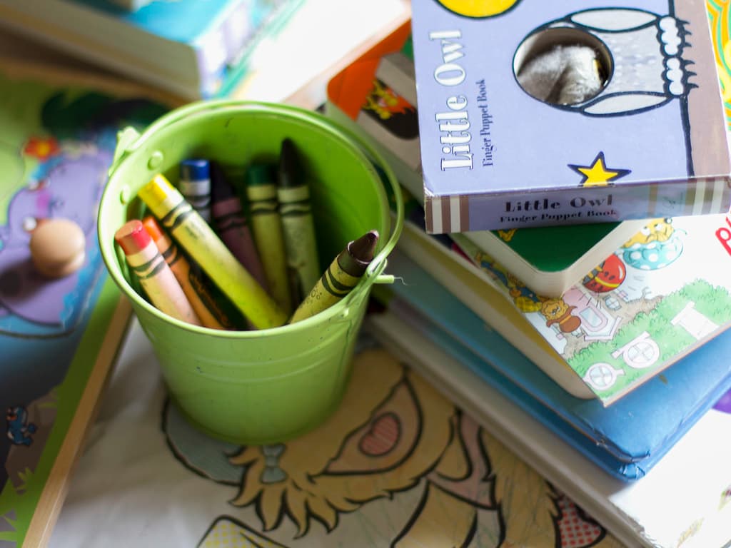 Giz de cera e livros infantis coloridos sobre uma mesa.